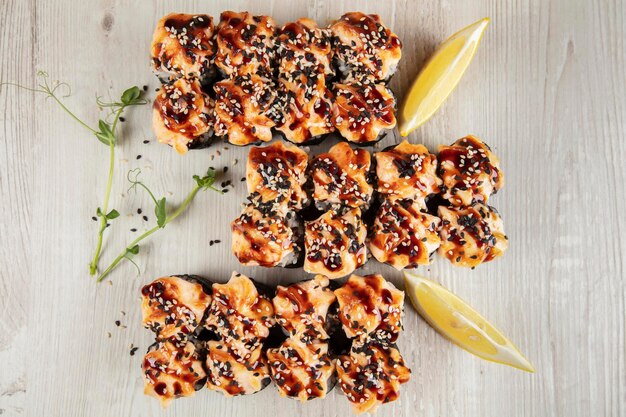 Un ensemble de rouleaux de sushi cuits au four saupoudré de graines de sésame sur un fond en bois blanc