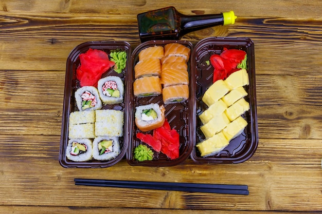 Ensemble de rouleaux de sushi dans des boîtes en plastique sauce soja et baguettes sur table en bois Vue de dessus