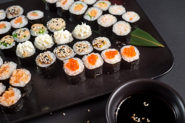 Ensemble de rouleaux de sushi japonais servi sur plaque noire sur fond sombre