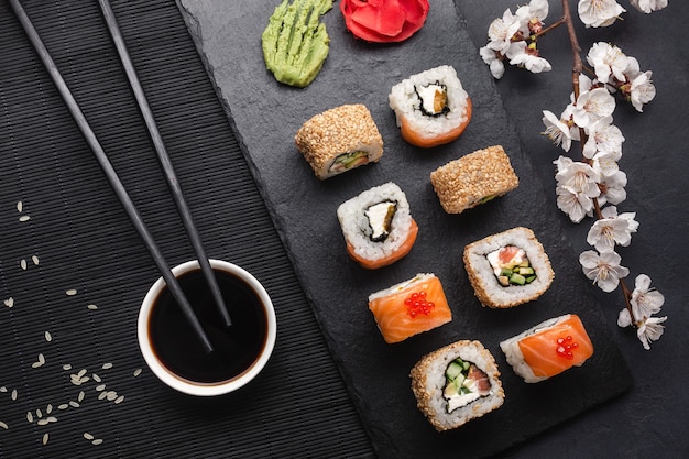 Ensemble de rouleaux de sushi et maki avec branche de fleurs blanches sur table en pierre. Vue de dessus.