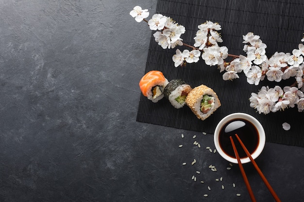 Ensemble de rouleaux de sushi et maki avec branche de fleurs blanches sur table en pierre. Vue de dessus.