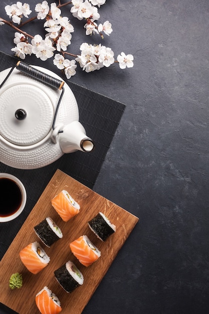 Ensemble De Rouleaux De Sushi Et Maki Avec Branche De Fleurs Blanches Et Théière Avec L'inscription Thé Vert Sur Table En Pierre. Vue De Dessus.