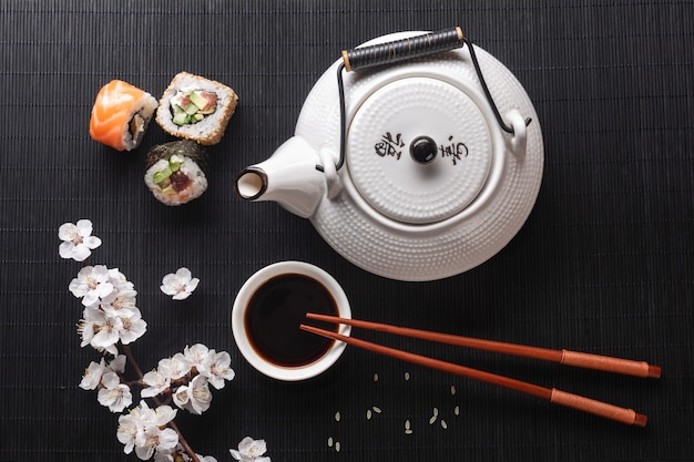 Ensemble de rouleaux de sushi et maki avec branche de fleurs blanches et théière avec l'inscription thé vert sur table en pierre. Vue de dessus.