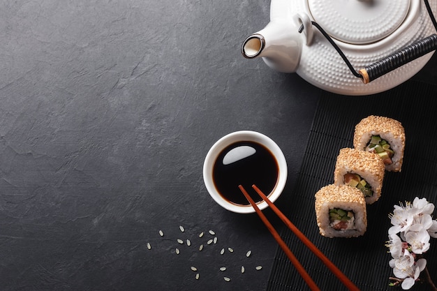 Ensemble de rouleaux de sushi et maki avec branche de fleurs blanches et théière sur table en pierre. Vue de dessus.