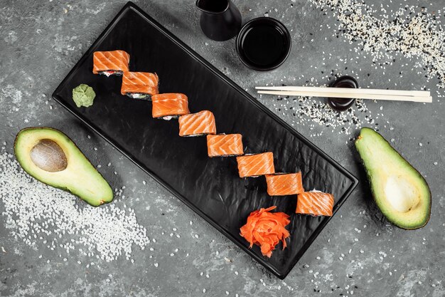 Un ensemble de rouleaux de sushi Philadelphia avec poisson rouge, fromage à la crème et montée noire se trouve dans un bateau en assiette. Rouleaux de sushi sur fond gris.