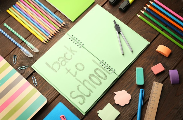 Ensemble scolaire avec inscription de retour à l'école dans un cahier et papeterie sur fond de bois