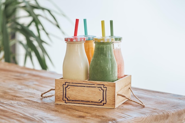 Ensemble de smoothies sains servis dans des bouteilles en verre avec des pailles colorées dans une boîte en bois sur la table