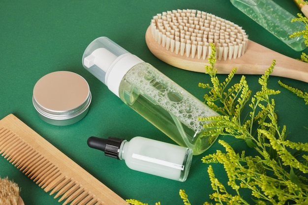 Ensemble de soins capillaires pour femmes peigne brosse en bois pot de gel flacon compte-gouttes sur fond vert vue de dessus