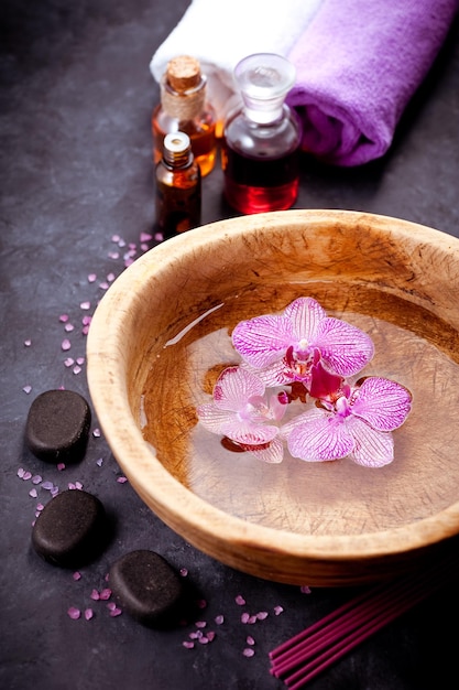 Ensemble spa Fleurs d'orchidées dans un bol avec des pierres zen d'eau et des huiles de massage