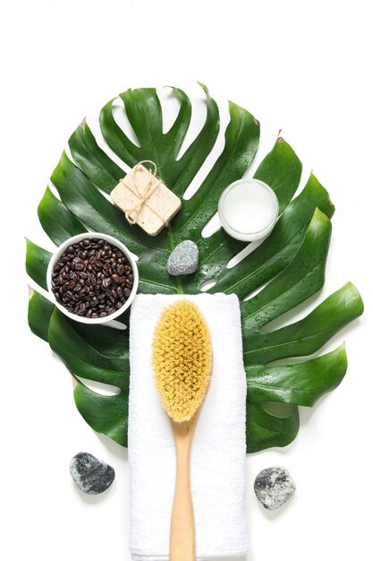 Ensemble SPA pour l'élimination de la cellulite, brosse dure cacius, grains de café, savon, serviette, feuille de monstera décorée. Vue d'en-haut. Format vertical.