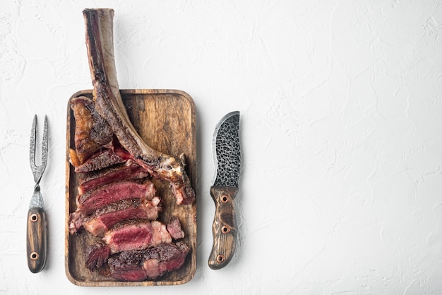 Ensemble de steak de boeuf tomahawk en tranches grillées, sur planche de service en bois, sur table en pierre blanche, vue de dessus à plat