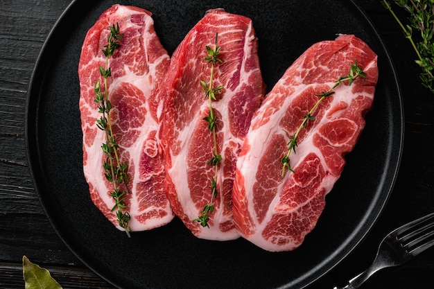 Ensemble de steak coupé au cou de porc cru, sur fond de table en bois noir, vue de dessus à plat