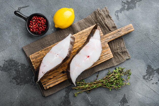 Ensemble de steak cru de poisson blanc, avec des ingrédients et des herbes de romarin, sur fond de table en pierre grise, vue de dessus à plat, avec espace de copie pour le texte