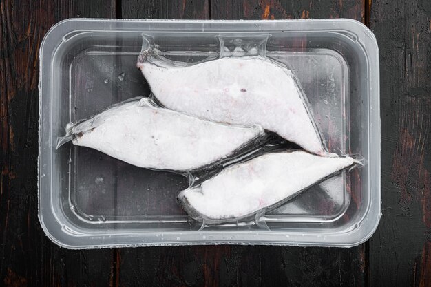 Ensemble de steaks congelés de poisson de flétan, sur fond de table en bois foncé ancien, vue de dessus à plat