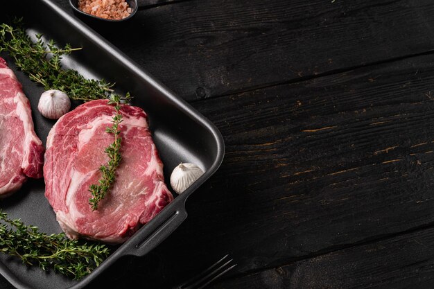 Ensemble de steaks de viande crue, sur fond de table en bois noir, vue de dessus à plat, avec espace de copie pour le texte