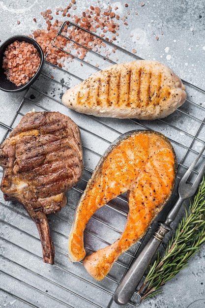 Ensemble de steaks de viande grillés au barbecue saumon boeuf et dinde sur un gril Fond gris Vue de dessus