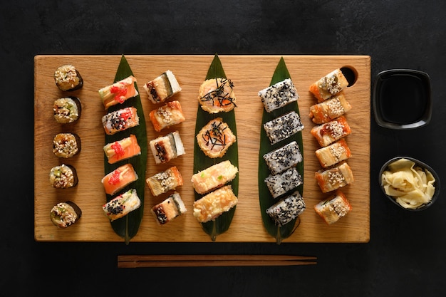 Ensemble de sushi servi sur une planche à découper en bois sur une surface noire. Vue d'en-haut. Style plat.