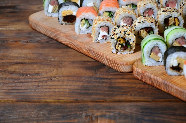 Un ensemble de sushis composé de plusieurs rouleaux se trouve sur une planche à découper en bois posée sur une table dans la cuisine d’un bar à sushis.