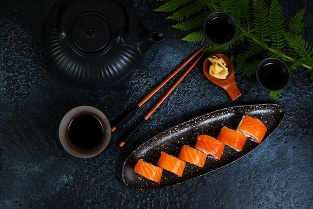 Un ensemble de sushis roule Philadelphie avec du poisson rouge et du fromage à la crème se trouve dans une assiette. Rouleaux de sushi sur fond noir avec une théière de thé chinois. Vue de dessus