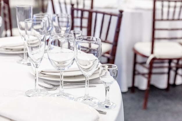 Ensemble de table de fantaisie pour le dîner avec des verres de serviette au restaurant, arrière-plan intérieur de luxe. Décoration de banquet élégante de mariage et articles pour la nourriture organisés par le service de restauration sur une table en nappe blanche.