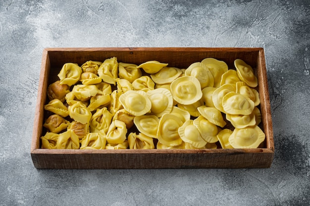 Ensemble de tortellini et raviolis faits à la main crue italienne, dans une boîte en bois, sur table grise