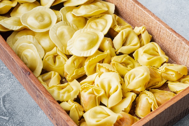 Ensemble de tortellini et raviolis italiens faits à la main, dans une boîte en bois, sur une table grise