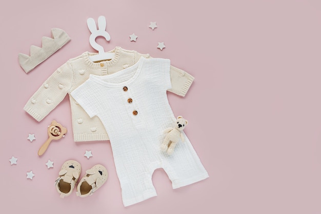 Ensemble de vêtements et accessoires pour bébé sur fond rose. Pull tricoté sur un joli cintre avec un body et des chaussures blancs, une couronne en coton et des jouets. Nouveau-né de mode. Mise à plat, vue de dessus