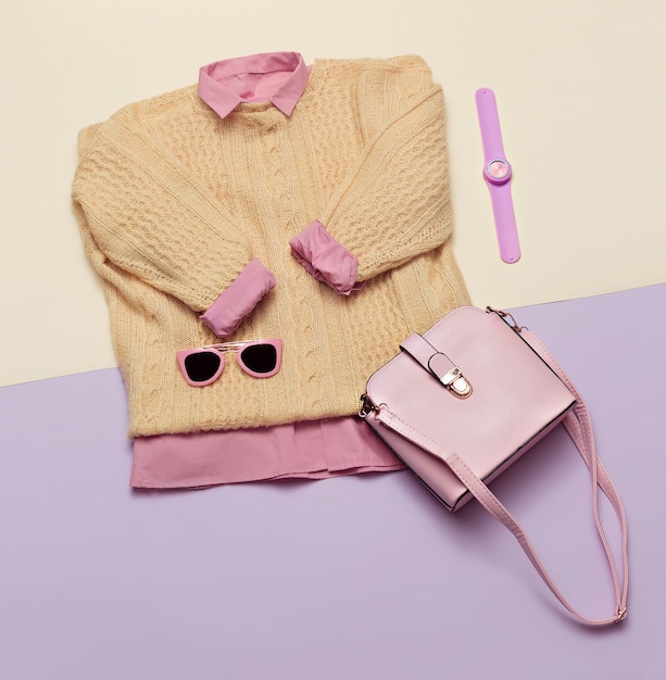 Ensemble de vêtements féminins élégants. Tenue femme/fille sur fond élégant. Couleur rose. Sacs à main, lunettes de soleil, montres. Pull et chemise Mise à plat, vue de dessus.