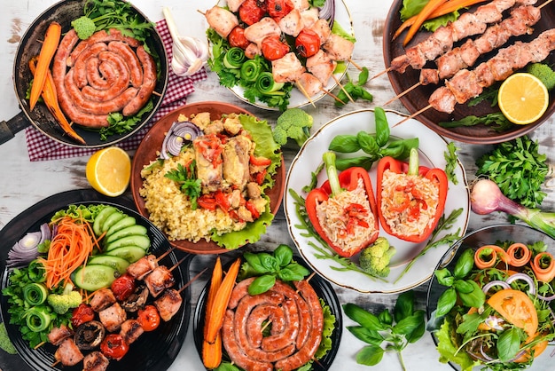 Un ensemble de viande barbecue Brochettes de saucisses Légumes frais Tomates Oignons Ail Sur un fond en bois blanc Espace de copie