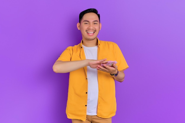 Enthousiaste beau jeune homme asiatique jetant des billets de banque isolés sur fond violet
