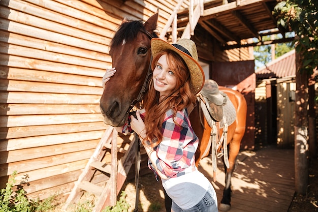 Enthousiaste belle jeune femme cowgirl avec son cheval sur ranch