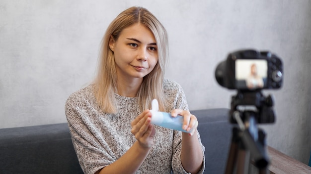 Enthousiaste blogueuse beauté féminine enregistrement vidéo à la maison. Elle montre une lotion pour la peau.