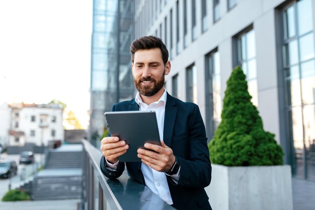 Enthousiaste confiant séduisant jeune homme de race blanche avec barbe en costume discutant sur tablette a réunion en plein air