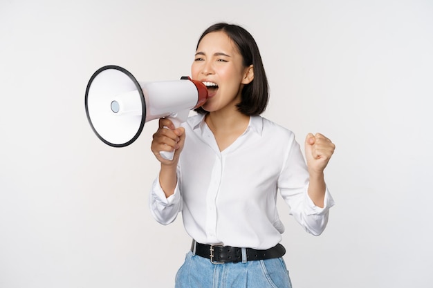 Enthousiaste femme asiatique fille activiste criant lors d'une manifestation à l'aide d'un mégaphone à l'air confiant de parler dans un haut-parleur protestant debout sur fond blanc