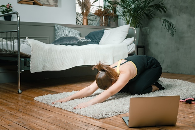 Enthousiaste femme sportive aux cheveux noirs s'étire jusqu'à la jambe dans la chambre