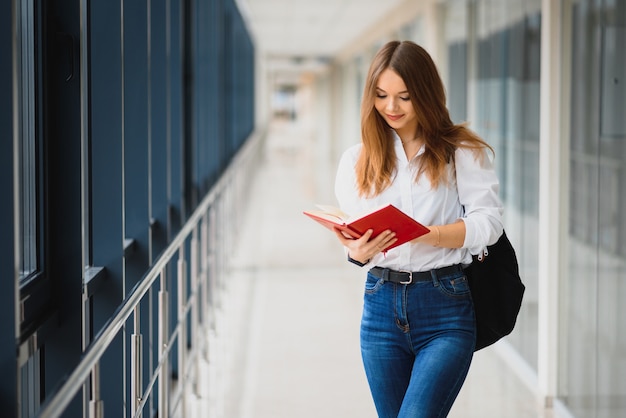Enthousiaste fille étudiante brune avec sac à dos noir détient des livres dans un bâtiment moderne