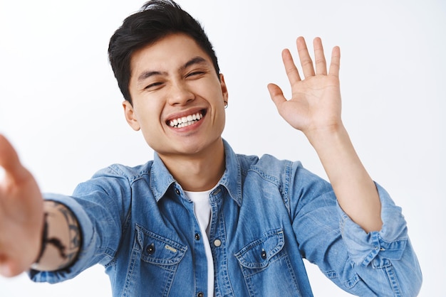 Enthousiaste heureux homme asiatique enthousiaste riant souriant en parlant à un ami appel vidéo via un téléphone portable souriant joyeusement en agitant la main pour saluer les abonnés en disant bonjour ou bonjour fond blanc