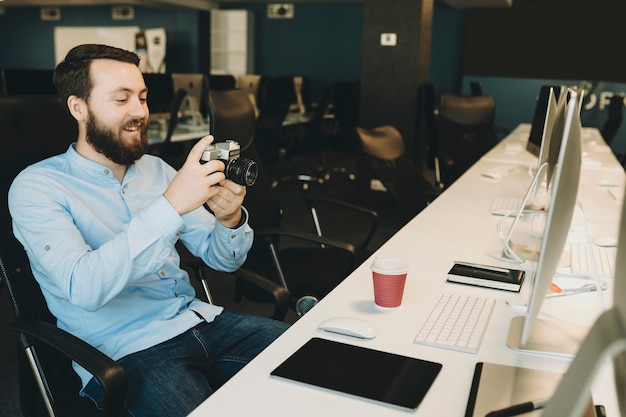 Enthousiaste homme adulte assis et défilement appareil photo au bureau au bureau