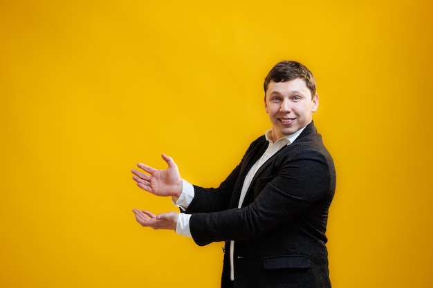 Enthousiaste homme d'affaires souriant portant un costume debout pointant les mains de côté sur l'espace de copie maquette sur fond de studio jaune