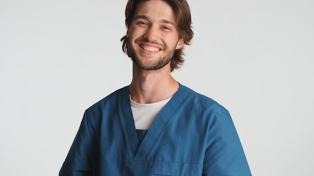 Enthousiaste homme médecin souriant à la caméra sur fond blanc Stagiaire attrayant habillé en uniforme à la recherche de travailleur médical isolé heureux