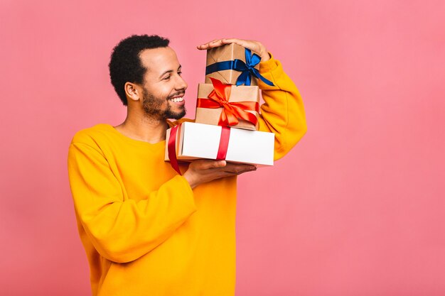 Enthousiaste homme souriant tenant des boîtes présentes emballées. Heureux jeune homme félicitant, donnant un cadeau d'anniversaire, isolé sur rose.