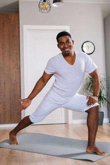 Enthousiaste instructeur de fitness afro-américain faisant de l'exercice sportif debout sur un tapis de yoga