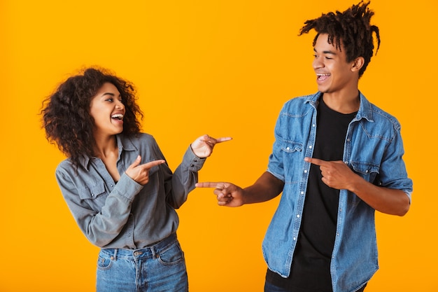 Photo enthousiaste jeune couple africain debout isolé, pointant du doigt les uns les autres