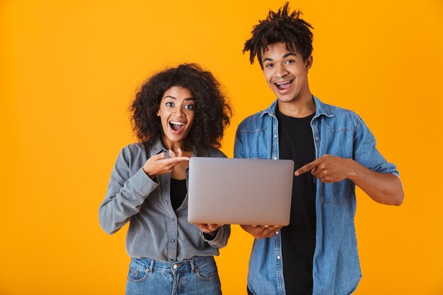 Enthousiaste jeune couple africain debout isolé, tenant un ordinateur portable, célébrant