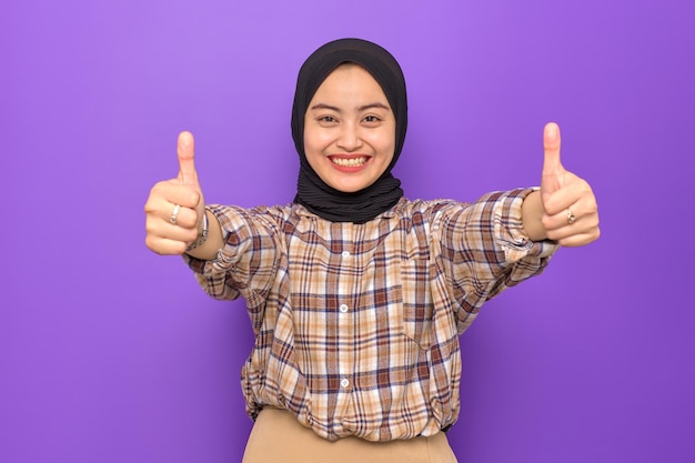 Enthousiaste jeune femme asiatique en chemise à carreaux montrant les pouces vers le haut isolé sur fond violet