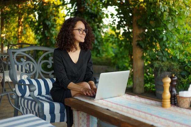 Enthousiaste jeune femme assise à la table en tapant sur l'ordinateur portable