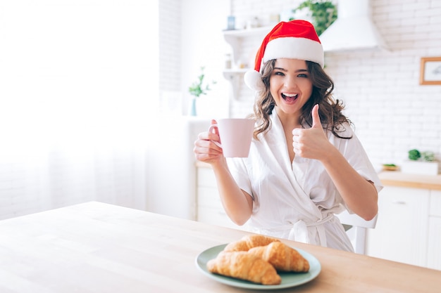 Enthousiaste jeune femme avec un chapeau rouge prendre le petit déjeuner le matin.