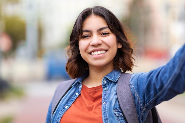 Enthousiaste jeune femme du Moyen-Orient prenant selfie à l'extérieur sur la rue de la ville