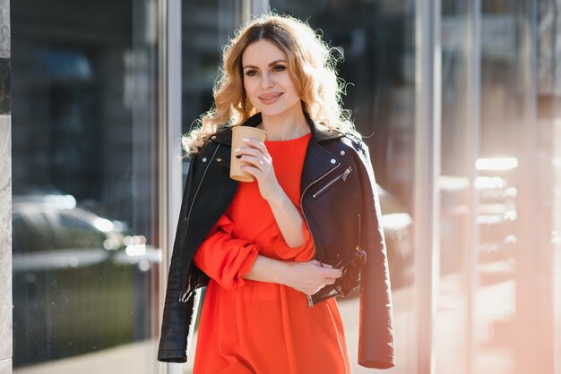 Enthousiaste jeune femme élégante dans la rue, boire du café du matin à la lumière du soleil.