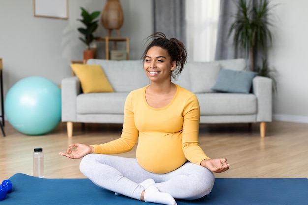 Enthousiaste jeune femme enceinte noire avec un gros ventre faisant des exercices pratiquant le yoga profiter du confort sportif et de la tranquillité